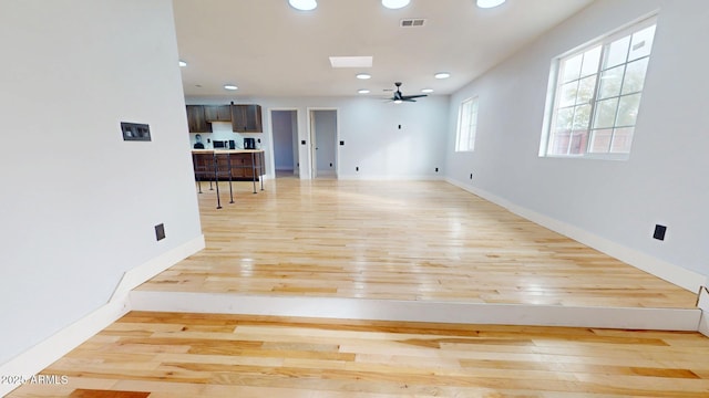 unfurnished living room with a skylight, ceiling fan, and light wood-type flooring