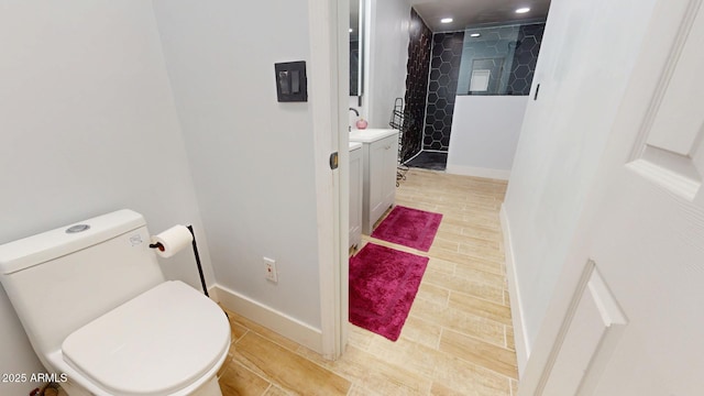 bathroom featuring hardwood / wood-style flooring, vanity, tiled shower, and toilet