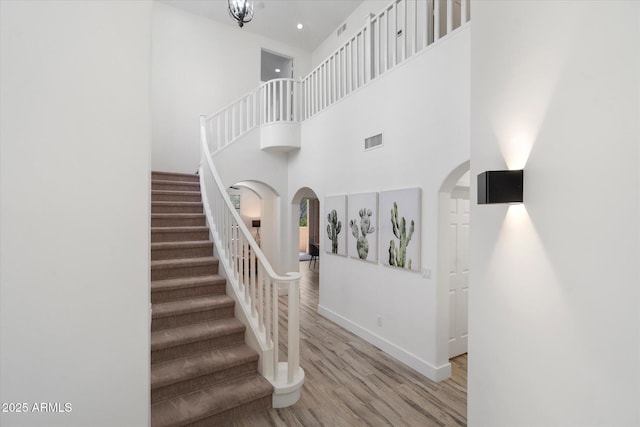 staircase featuring a towering ceiling, baseboards, visible vents, arched walkways, and wood finished floors