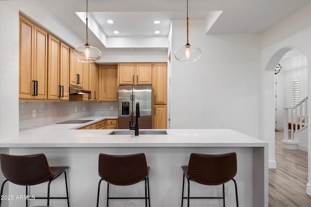 kitchen featuring stainless steel fridge with ice dispenser, arched walkways, a peninsula, under cabinet range hood, and decorative backsplash