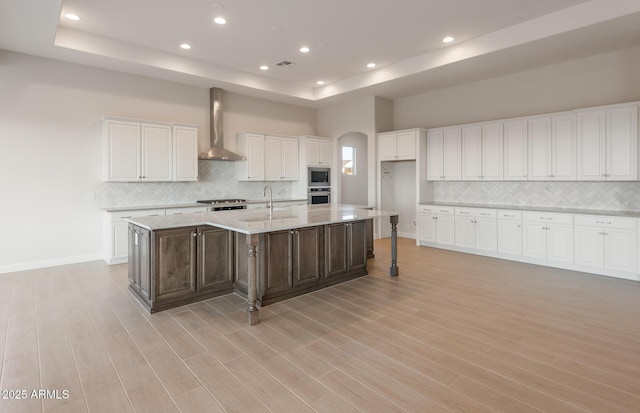 26696 W Siesta Ln, Buckeye, AZ 85396 - kitchen with a raised ceiling, light wood finished floors, a large island, white cabinets, and wall chimney exhaust hood