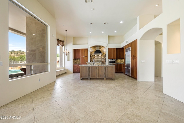 kitchen featuring arched walkways, brown cabinetry, stainless steel appliances, backsplash, and a notable chandelier
