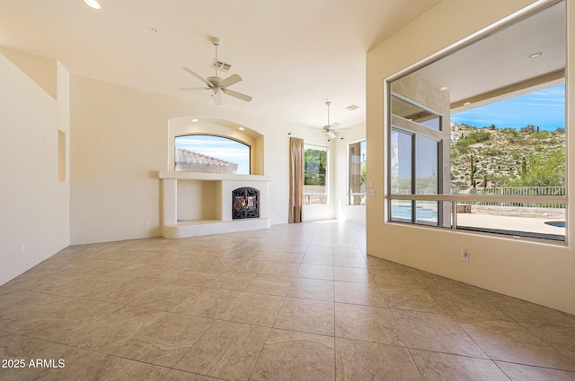 unfurnished living room featuring a ceiling fan, visible vents, a wealth of natural light, and a warm lit fireplace