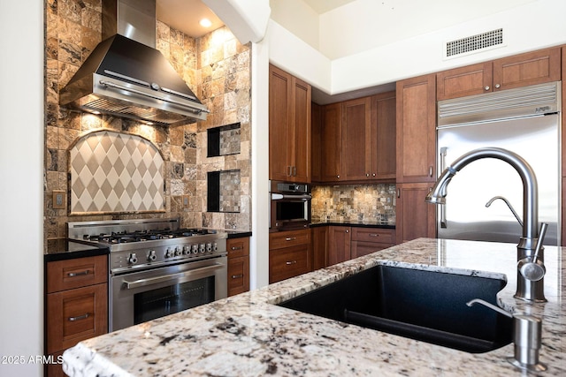 kitchen with wall chimney range hood, visible vents, premium appliances, and backsplash