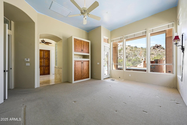 unfurnished living room with visible vents, arched walkways, ceiling fan, and light colored carpet