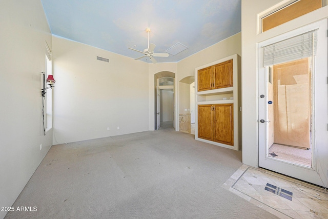 unfurnished living room with arched walkways, visible vents, a ceiling fan, and light carpet