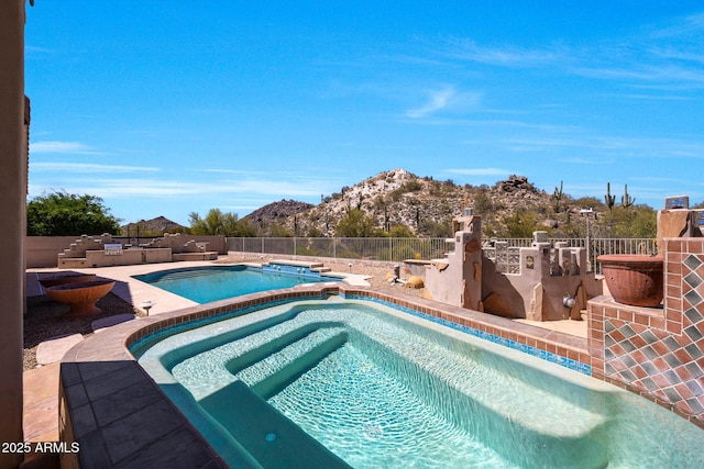 view of swimming pool featuring a mountain view, a patio, a pool with connected hot tub, and fence