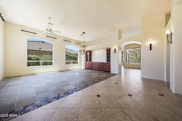 tiled empty room with a wealth of natural light, arched walkways, and ceiling fan with notable chandelier