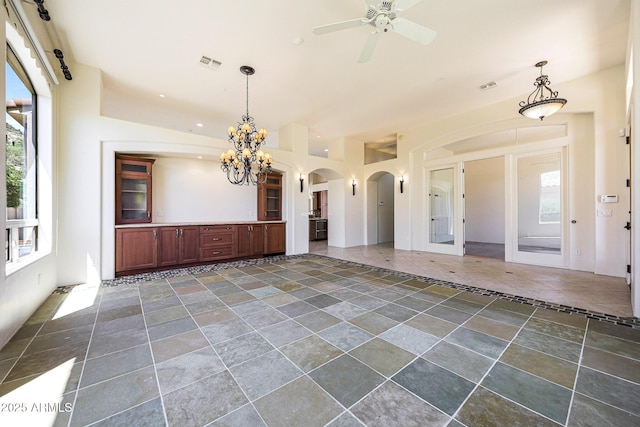 unfurnished living room featuring visible vents, arched walkways, ceiling fan with notable chandelier, and stone tile flooring