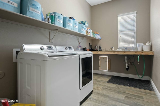 laundry area featuring washer and dryer, a sink, light wood-type flooring, laundry area, and baseboards