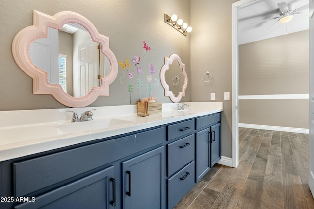 bathroom featuring double vanity, a ceiling fan, a sink, wood finished floors, and baseboards