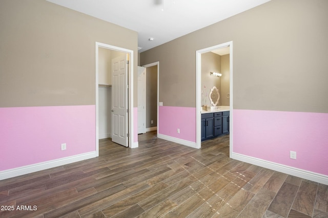 unfurnished bedroom featuring a walk in closet, a closet, baseboards, and wood finished floors