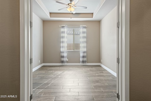 empty room featuring ceiling fan, a tray ceiling, baseboards, and wood finish floors