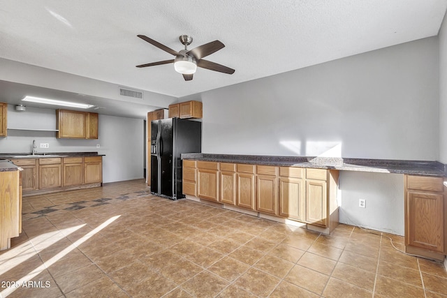 kitchen featuring sink, light tile patterned floors, ceiling fan, black fridge, and a textured ceiling