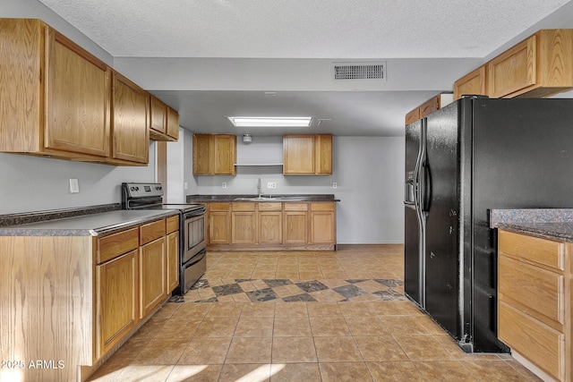 kitchen with stainless steel electric range oven, sink, light tile patterned floors, black fridge, and a textured ceiling