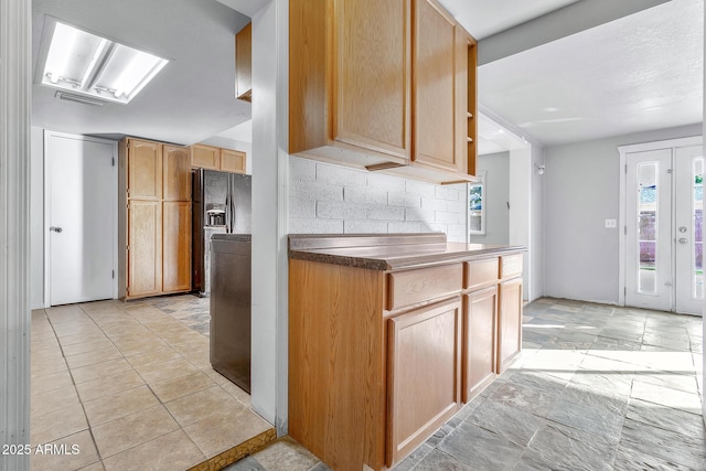 kitchen featuring black fridge with ice dispenser, decorative backsplash, and light brown cabinets