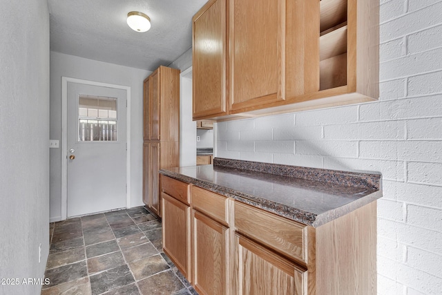 kitchen featuring a textured ceiling, light brown cabinetry, and dark stone counters