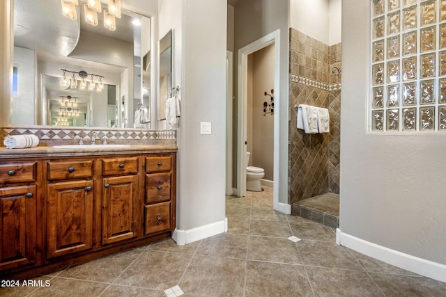 bathroom featuring tasteful backsplash, tile patterned flooring, toilet, tiled shower, and vanity