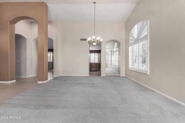 carpeted empty room with vaulted ceiling and an inviting chandelier