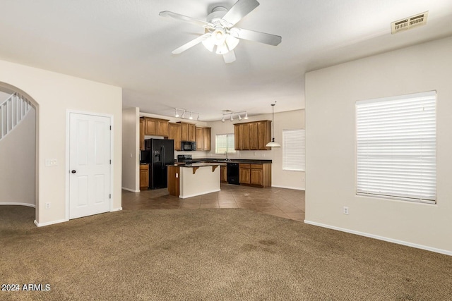 unfurnished living room with dark colored carpet, rail lighting, ceiling fan, and sink