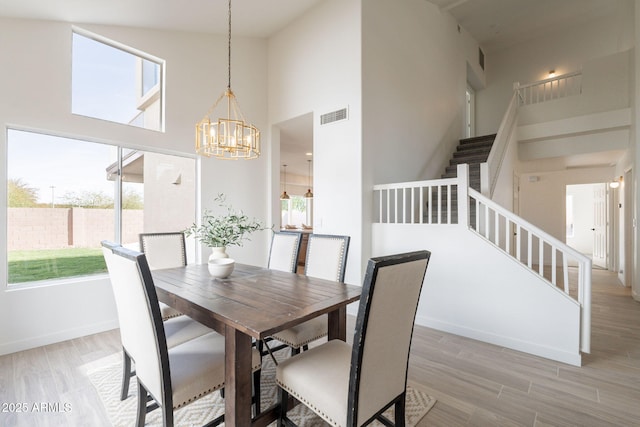 3837 E Windsong Dr, Phoenix, AZ 85048 - dining area featuring stairs, healthy amount of natural light, a chandelier, a high ceiling, and light wood-style floors