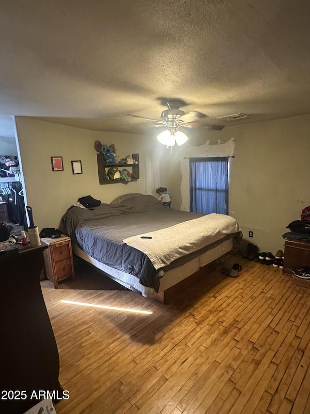 bedroom with a textured ceiling, visible vents, light wood-style flooring, and a ceiling fan