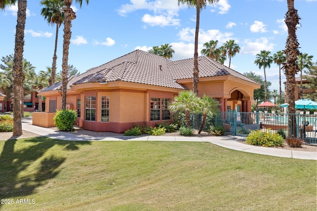 view of front of house with fence, a tiled roof, a front lawn, and stucco siding