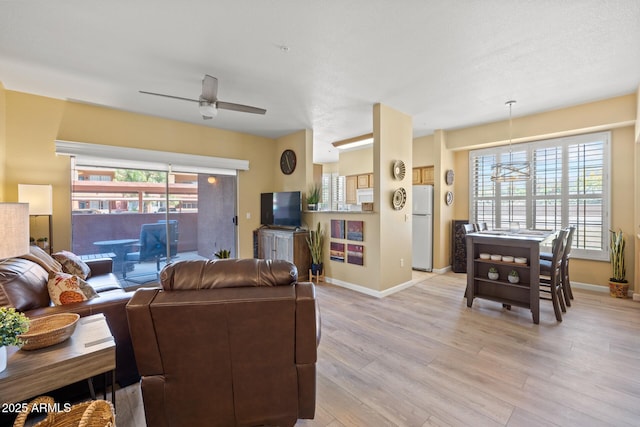 living area featuring a ceiling fan, baseboards, plenty of natural light, and light wood-type flooring