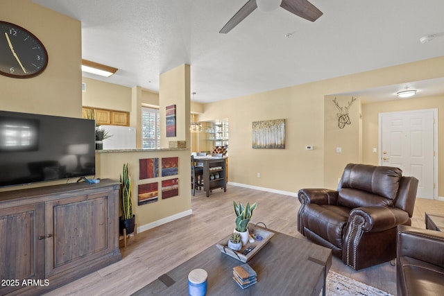 living room featuring baseboards, a ceiling fan, and light wood finished floors