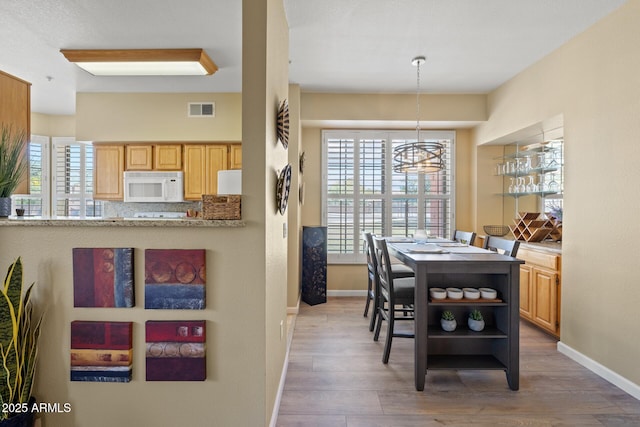 dining room with a notable chandelier, baseboards, visible vents, and wood finished floors