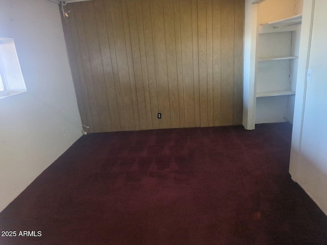 unfurnished room with wooden walls and dark colored carpet