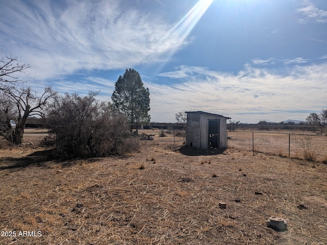 view of yard featuring a storage shed, fence, an outdoor structure, and a rural view