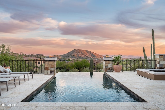 pool at dusk featuring a fenced in pool, a mountain view, and a patio area