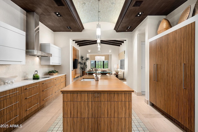 kitchen featuring modern cabinets, light countertops, black electric cooktop, wall chimney exhaust hood, and a sink