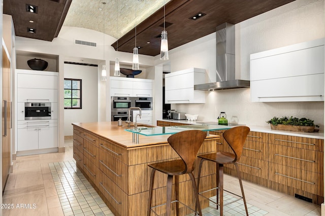 kitchen with light countertops, modern cabinets, wall chimney exhaust hood, and visible vents