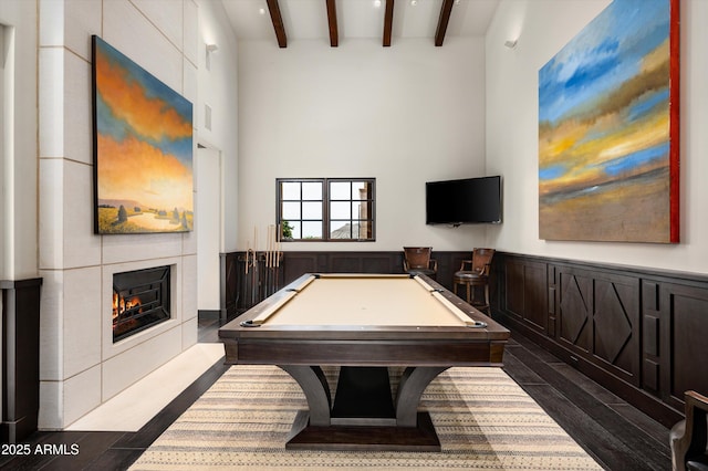 recreation room featuring a warm lit fireplace, dark wood finished floors, billiards, a towering ceiling, and beamed ceiling