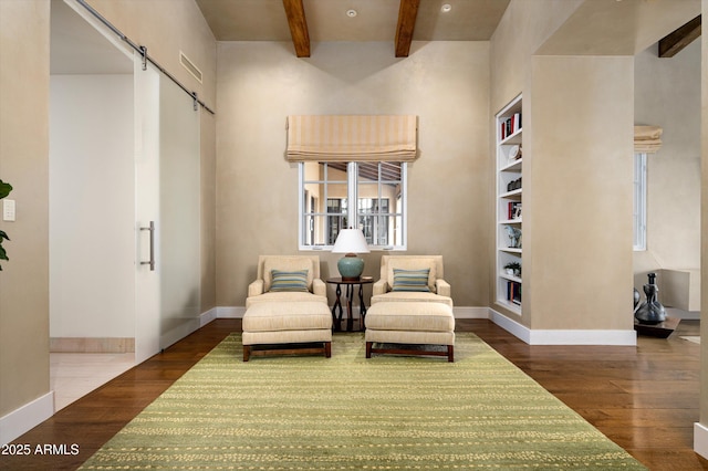 living area with a high ceiling, a barn door, beam ceiling, baseboards, and wood finished floors