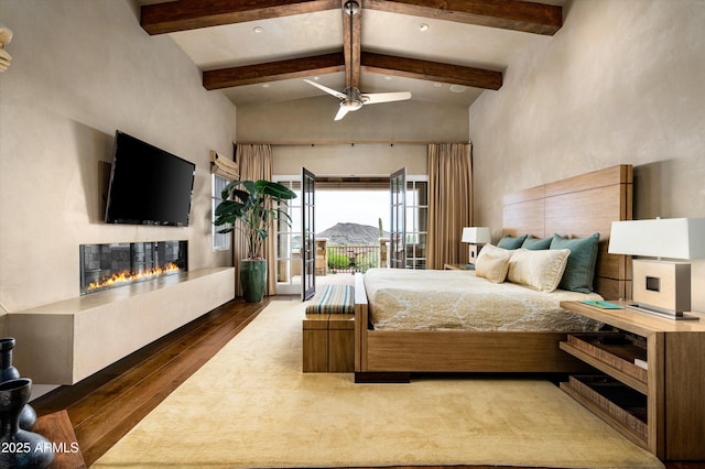 bedroom featuring a ceiling fan, wood finished floors, high vaulted ceiling, beamed ceiling, and a glass covered fireplace