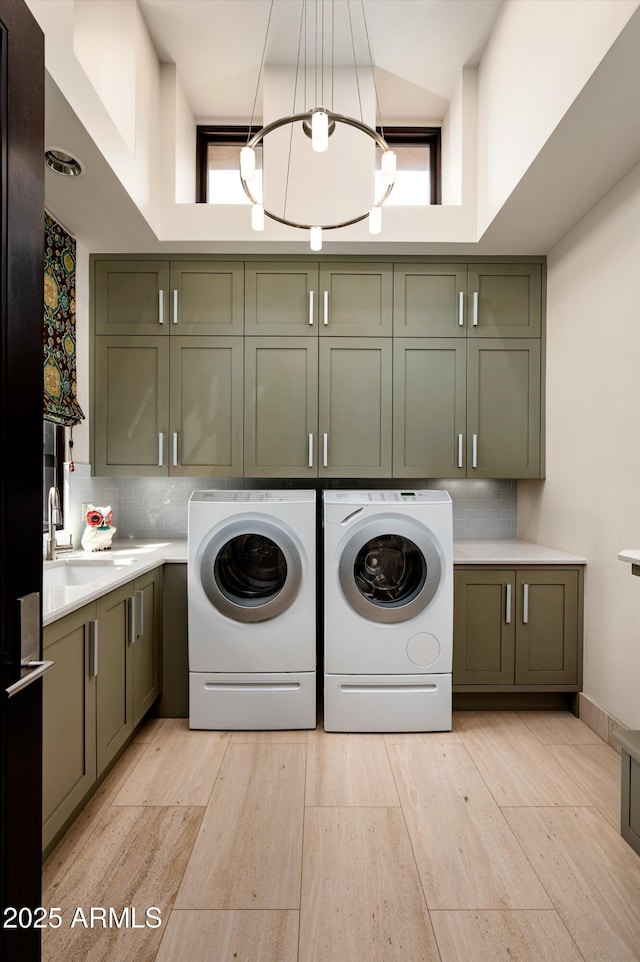 laundry area with cabinet space, a notable chandelier, a sink, separate washer and dryer, and light wood-type flooring