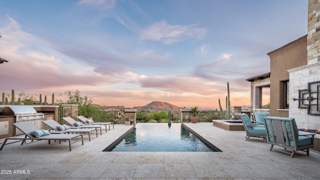 pool at dusk featuring area for grilling, exterior kitchen, a fenced in pool, and a patio