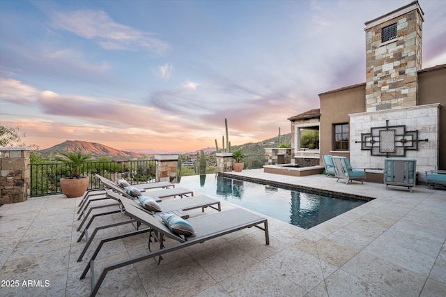 pool at dusk featuring a fenced in pool, a patio area, and a fireplace