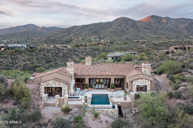 exterior space featuring stucco siding, an outdoor pool, a mountain view, a chimney, and a patio