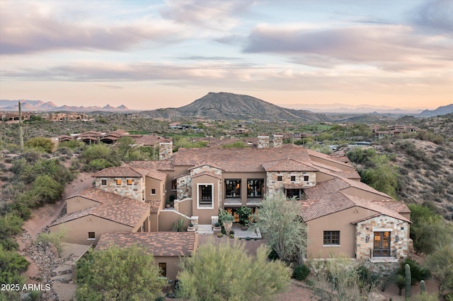view of front facade featuring a balcony, a mountain view, stone siding, and stucco siding