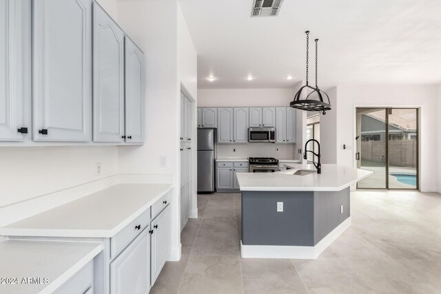 kitchen featuring light tile patterned floors, decorative light fixtures, appliances with stainless steel finishes, sink, and a center island with sink