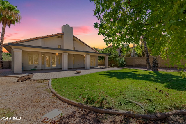 back house at dusk featuring a lawn and a patio area