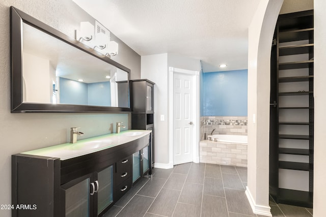 bathroom with tile patterned flooring, tiled tub, vanity, and a textured ceiling