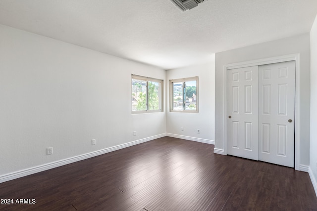 unfurnished bedroom featuring a textured ceiling, a closet, and dark wood-type flooring