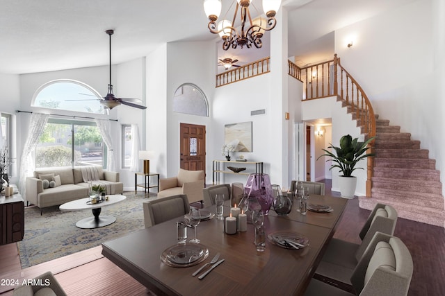 dining area with wood-type flooring, ceiling fan with notable chandelier, and a towering ceiling