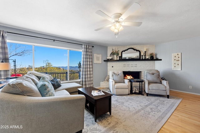 living room with a brick fireplace, wood-type flooring, and ceiling fan