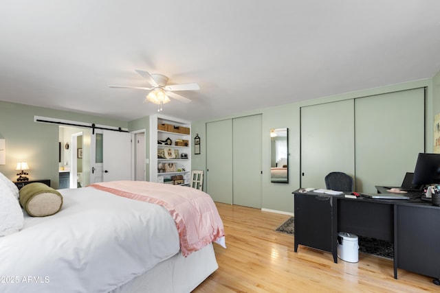 bedroom featuring multiple closets, ceiling fan, a barn door, and light wood-type flooring